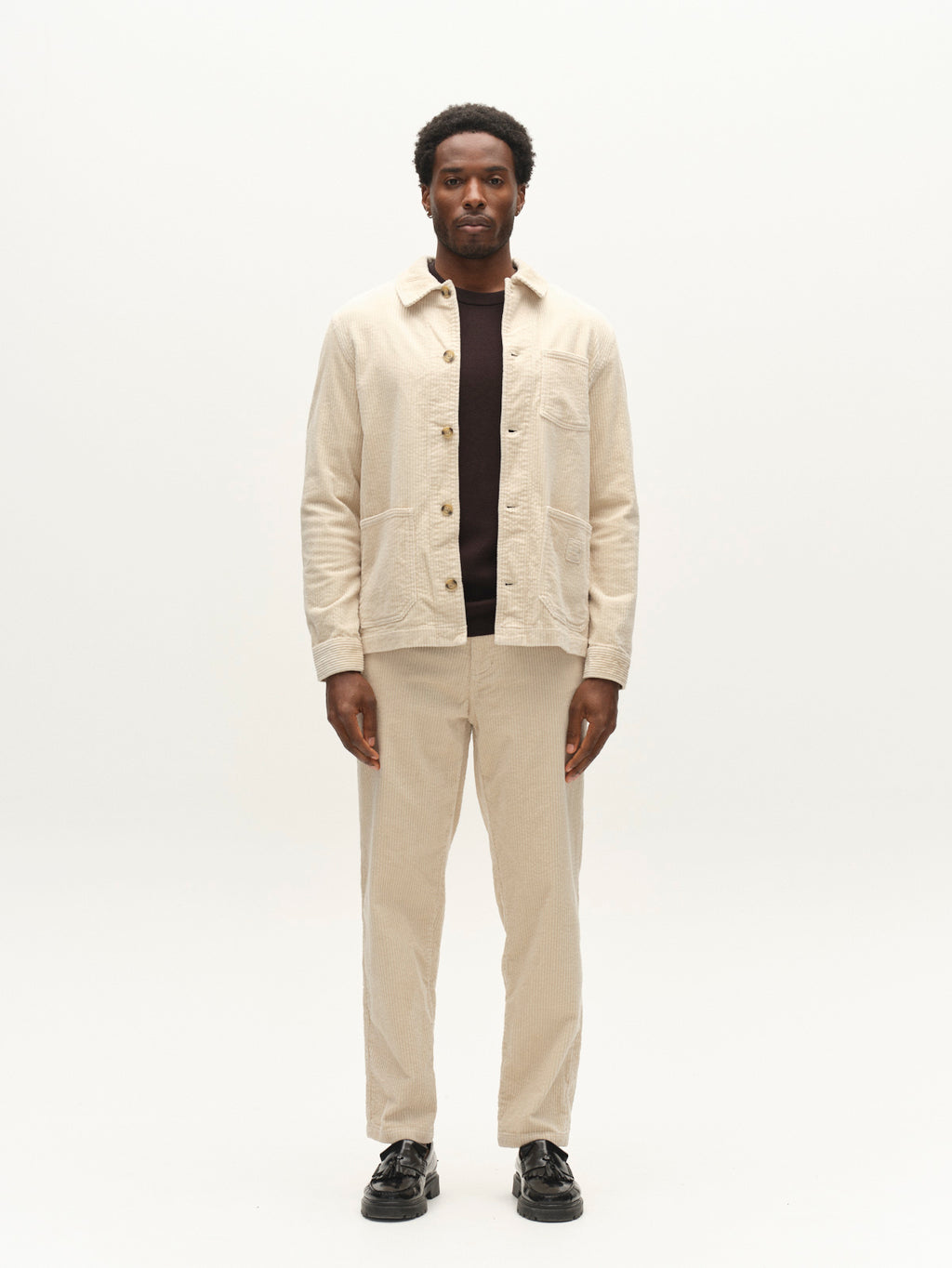 A man stands facing forward against a plain white background, wearing the Gabba GABbeta Ibre LS Overshirt in Birch with utility pockets, paired with matching pants over a dark shirt and black shoes.