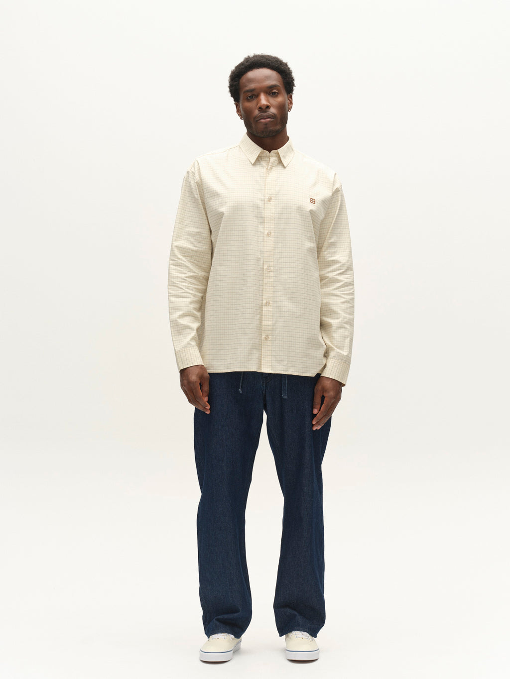A man stands against a plain background wearing the Gabba GABjens Over Indie LS Shirt in Lt. Sand, paired with dark blue pants and white sneakers. He faces forward with a neutral expression and relaxed posture.