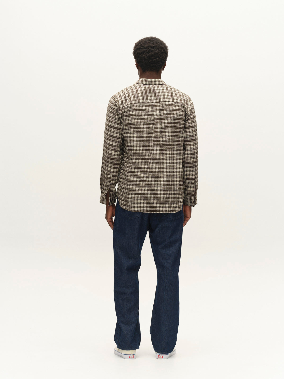 A person stands facing away from the camera, wearing the Gabba GABsven Reg TX2 LS Shirt in Forest Night—a regular fit, yarn-dyed cotton shirt with a checked texture—paired with blue jeans and white sneakers against a plain white background.