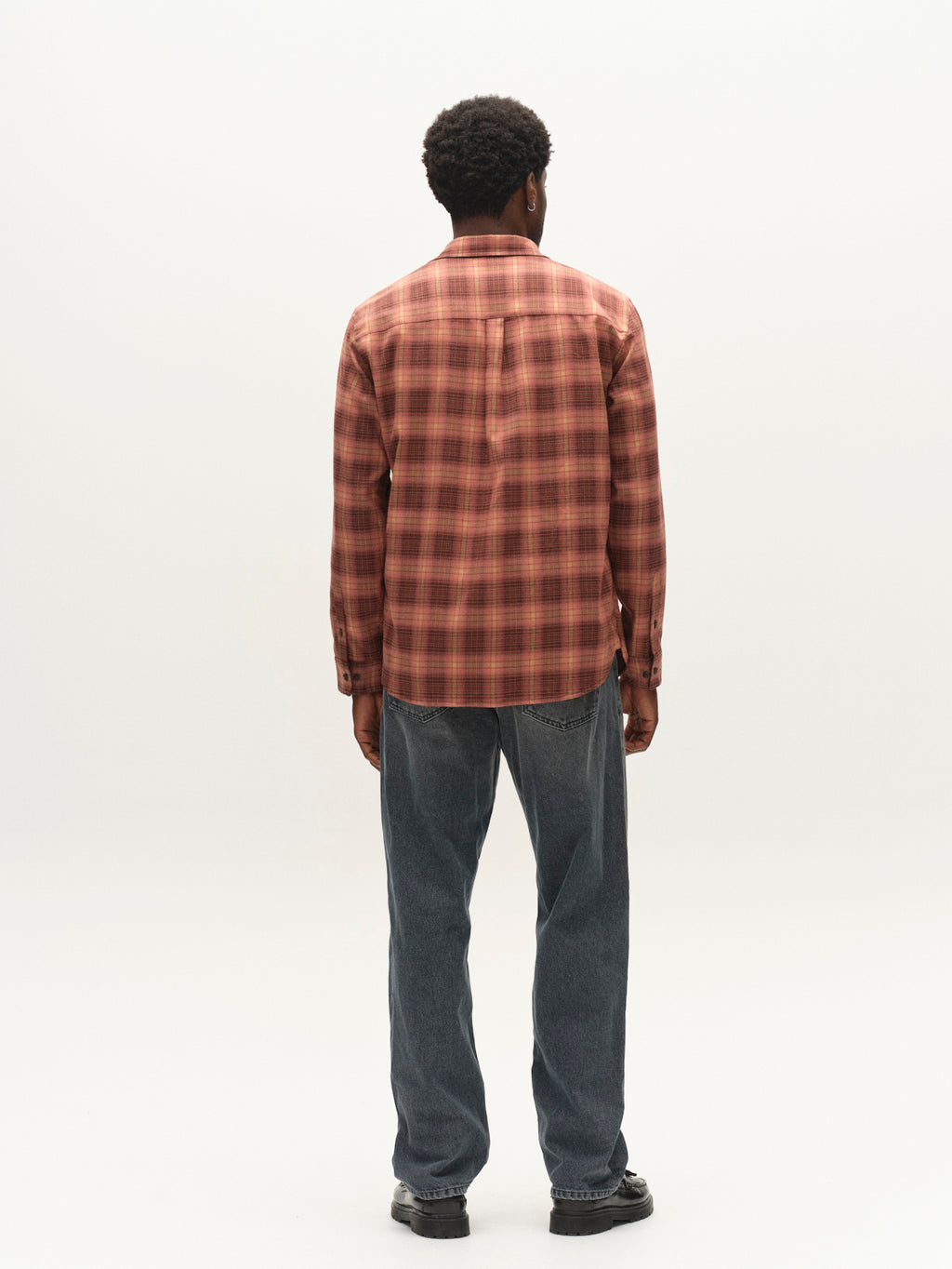 A man stands facing away, wearing the Gabba GABsven Reg F1097 LS Shirt in Brick Red with a checked texture, paired with blue jeans and black shoes, set against a plain white background.