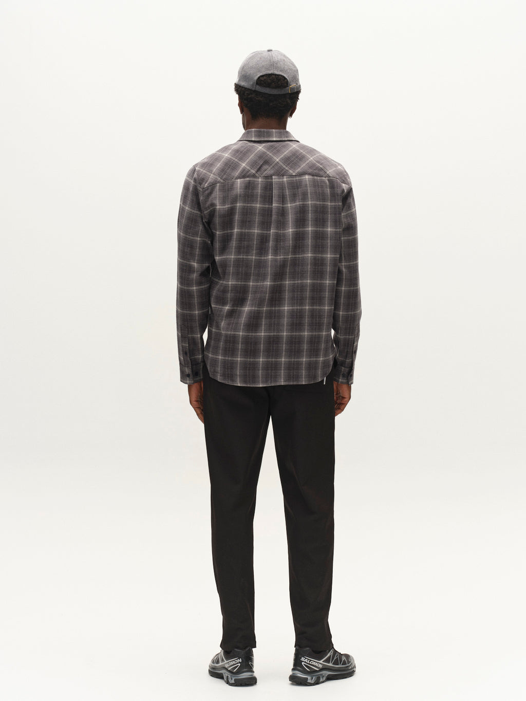 A person stands facing away, wearing the Gabba GABsven Reg F1097 LS Shirt in Night Sky, paired with dark pants, a light gray cap, and black-and-white sneakers against a plain light background.