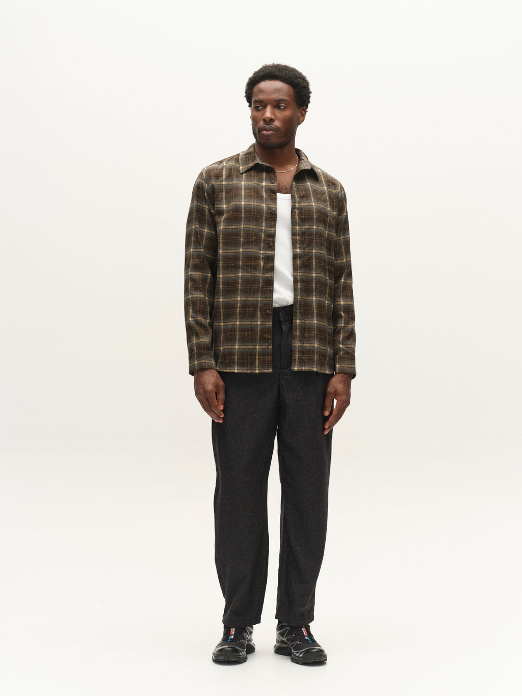 A man stands against a plain light background, wearing the Gabba GABsven Reg F1097 LS Shirt in Forest Night over a white shirt, paired with dark gray pants and black sneakers.