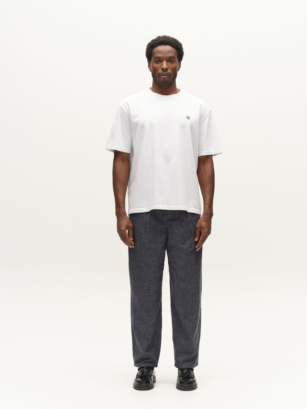 A man stands facing forward, wearing a plain white t-shirt, Gabba GABdavid Twilight Pant in navy with a loose tapered fit, and black shoes, against a plain white background.