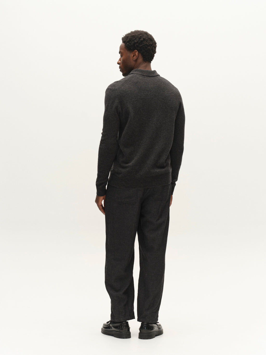 A man stands facing away, wearing a dark sweater, black shoes, and the Gabba GABdavid Twilight Pant in Dark Grey against a plain white background.