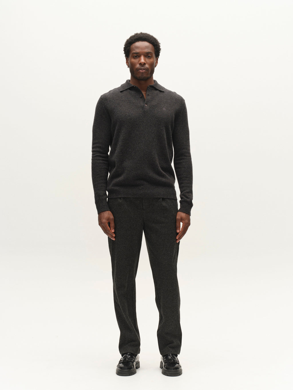 A man stands facing forward against a plain white background, wearing a dark long-sleeve polo shirt, black shoes, and Gabba’s GABnapoli 19 Zaffe GRS Pant in Dark Grey—regular straight fit trousers crafted from soft stretch fabric.