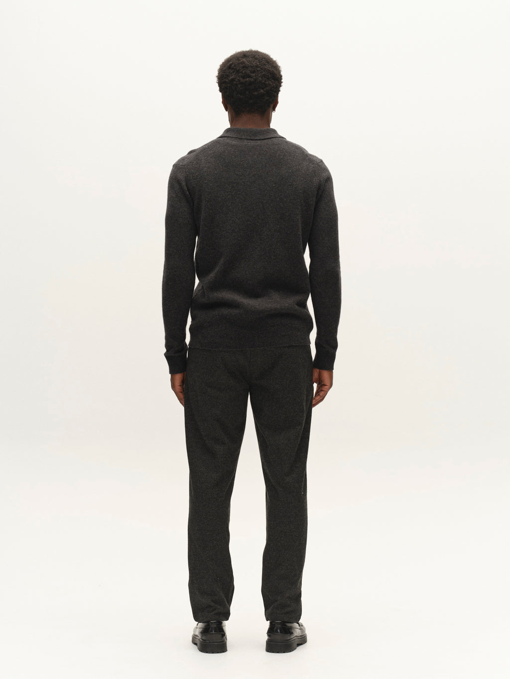 A man with short curly hair stands facing away, wearing a dark sweater, black shoes, and the Gabba GABnapoli 19 Zaffe GRS Pant in dark grey—regular straight fit trousers in a wool-look finish crafted from soft stretch fabric—against a plain white background.