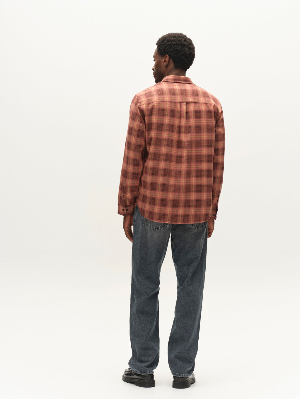 A man stands facing away, wearing a red plaid button-up shirt, Gabba GABnoah Primesto WW0030 Jeans in grey denim, and black shoes, against a plain white background.
