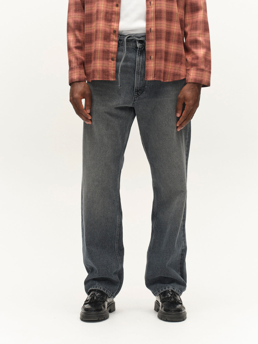 A person stands facing forward against a plain background, wearing a red plaid shirt, white t-shirt, and black shoes. They are also wearing Gabba GABnoah Primesto WW0030 Jeans in Grey Denim; their head is not visible in the image.