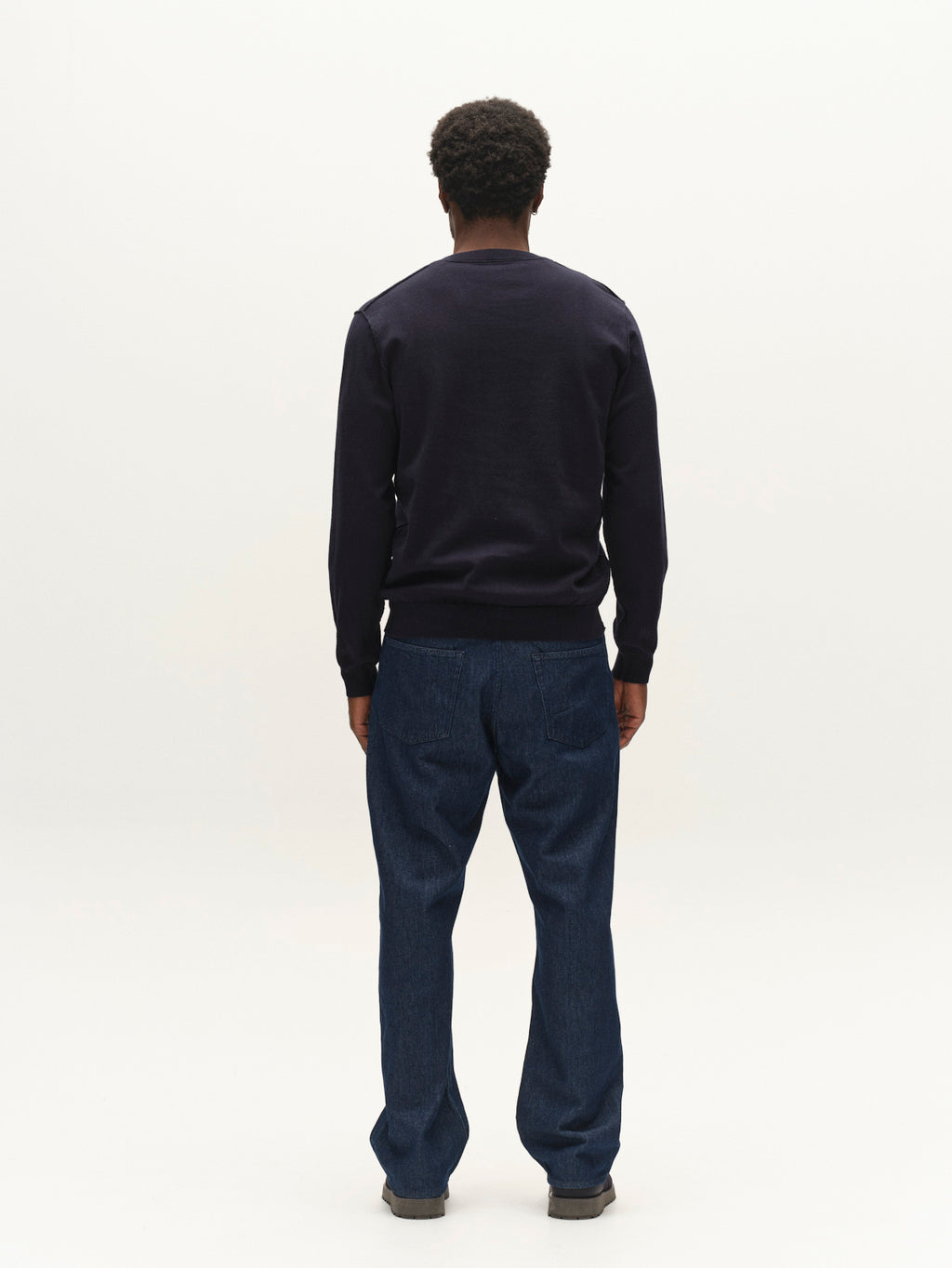 A person viewed from behind wearing a navy blue GABfumo Element Spy LS Knit crew neck sweater in a flat-knit cotton and dark blue jeans.
