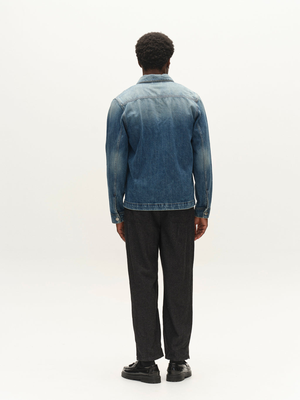A person stands facing away, wearing the Gabba GABbeta Wolv DS0004 LS Overshirt in dark blue denim, styled with dark pants and black shoes against a plain white background.