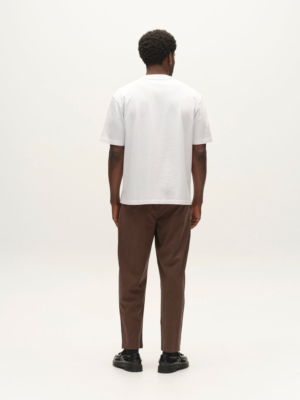 A man seen from behind wearing a white t-shirt, black loafers, and GABfirenze Bolu Cropped TENCEL ™ Pant - Brown Slate in stretch twill.