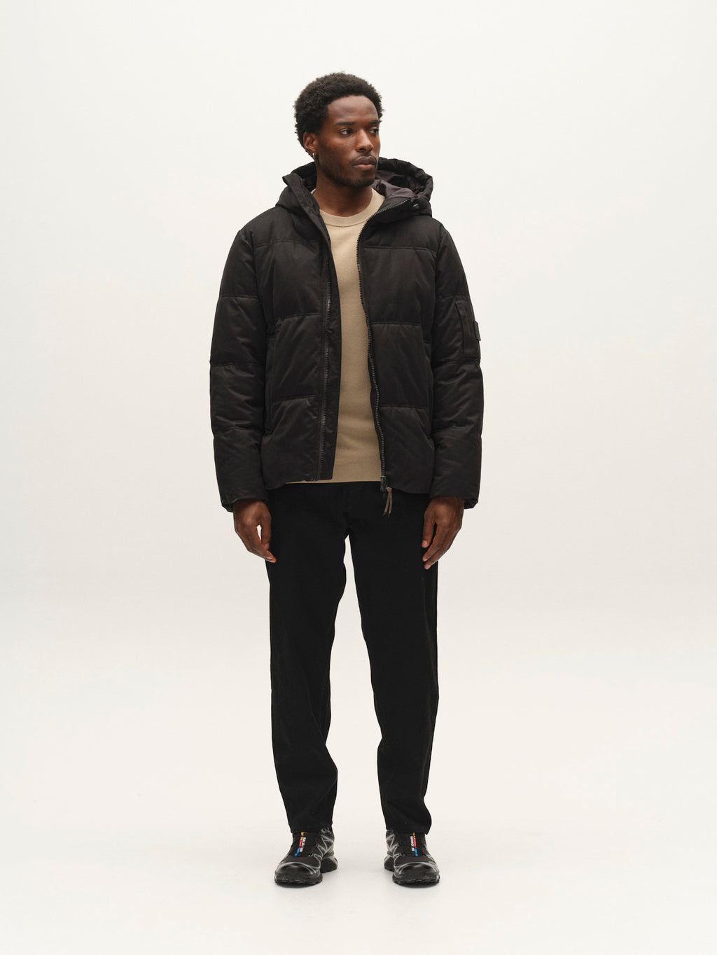 A man wearing a GABjulien Calle Outerwear - Black jacket, tan sweater, and black pants.
