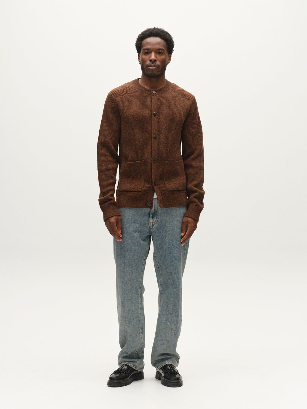 A man stands facing forward, wearing the Gabba GABremy Cardi Flash LS Knit in Brown Slate—a relaxed fit wool cardigan with rib-knit detailing—paired with light blue jeans and black shoes against a plain white background.