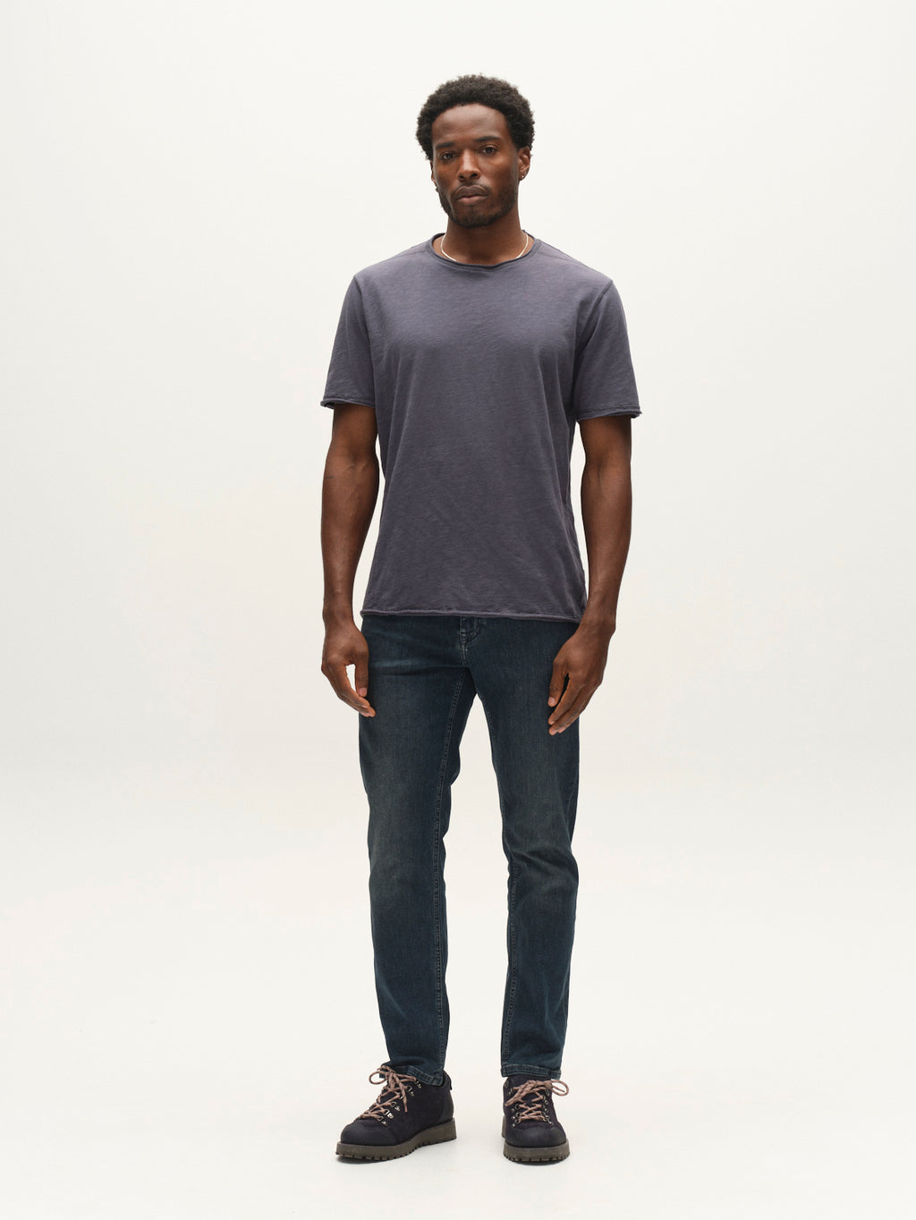 A man stands facing forward, wearing a dark gray t-shirt, Gabba GABmarc Nham RS2113 Jeans in dark blue denim, and dark shoes, against a plain white background.