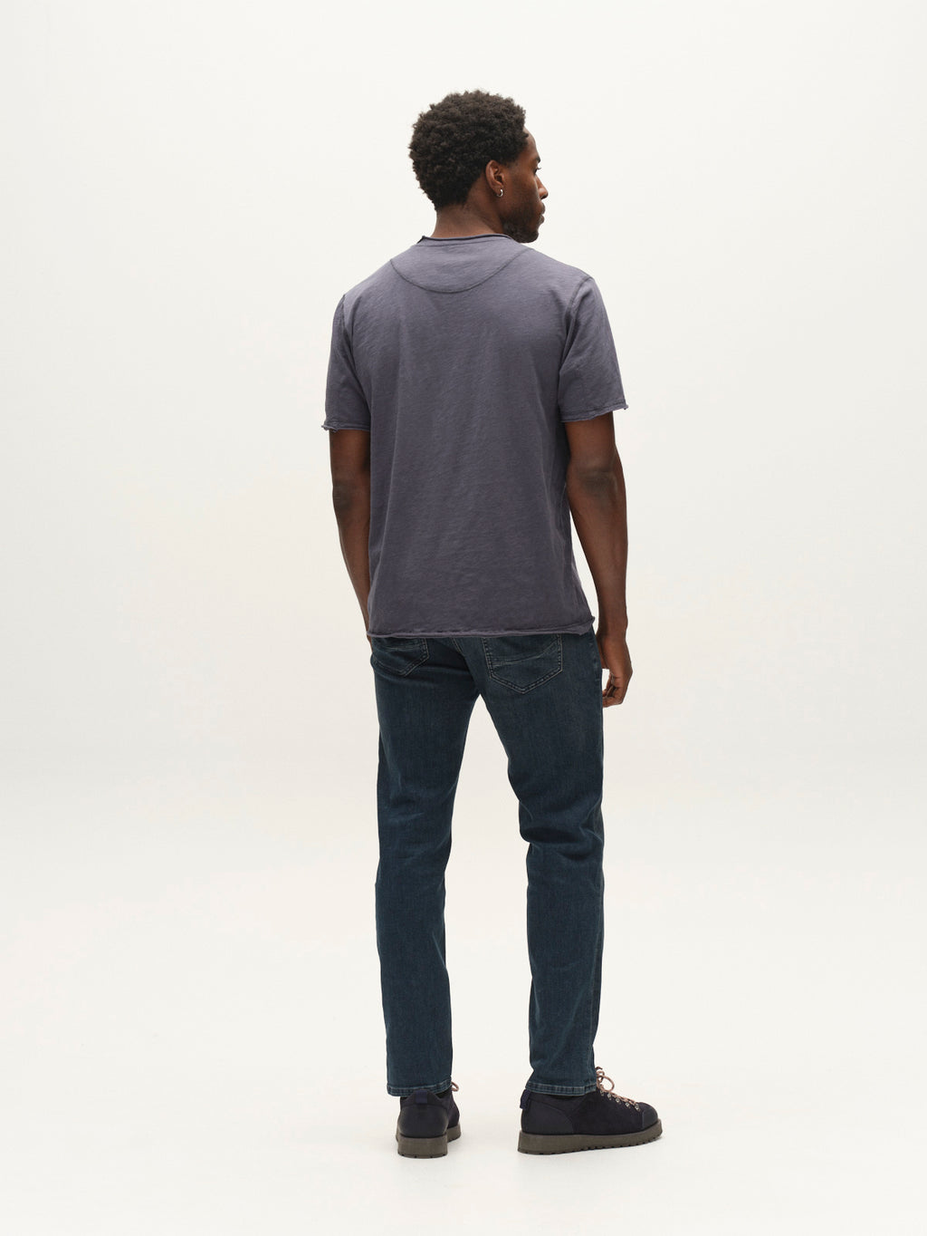 A man stands facing away from the camera, wearing a short-sleeve gray polo shirt, black shoes, and Gabba GABmarc Nham RS2113 Jeans in dark blue denim—crafted with performance comfort ISKO stretch denim—against a plain white background.