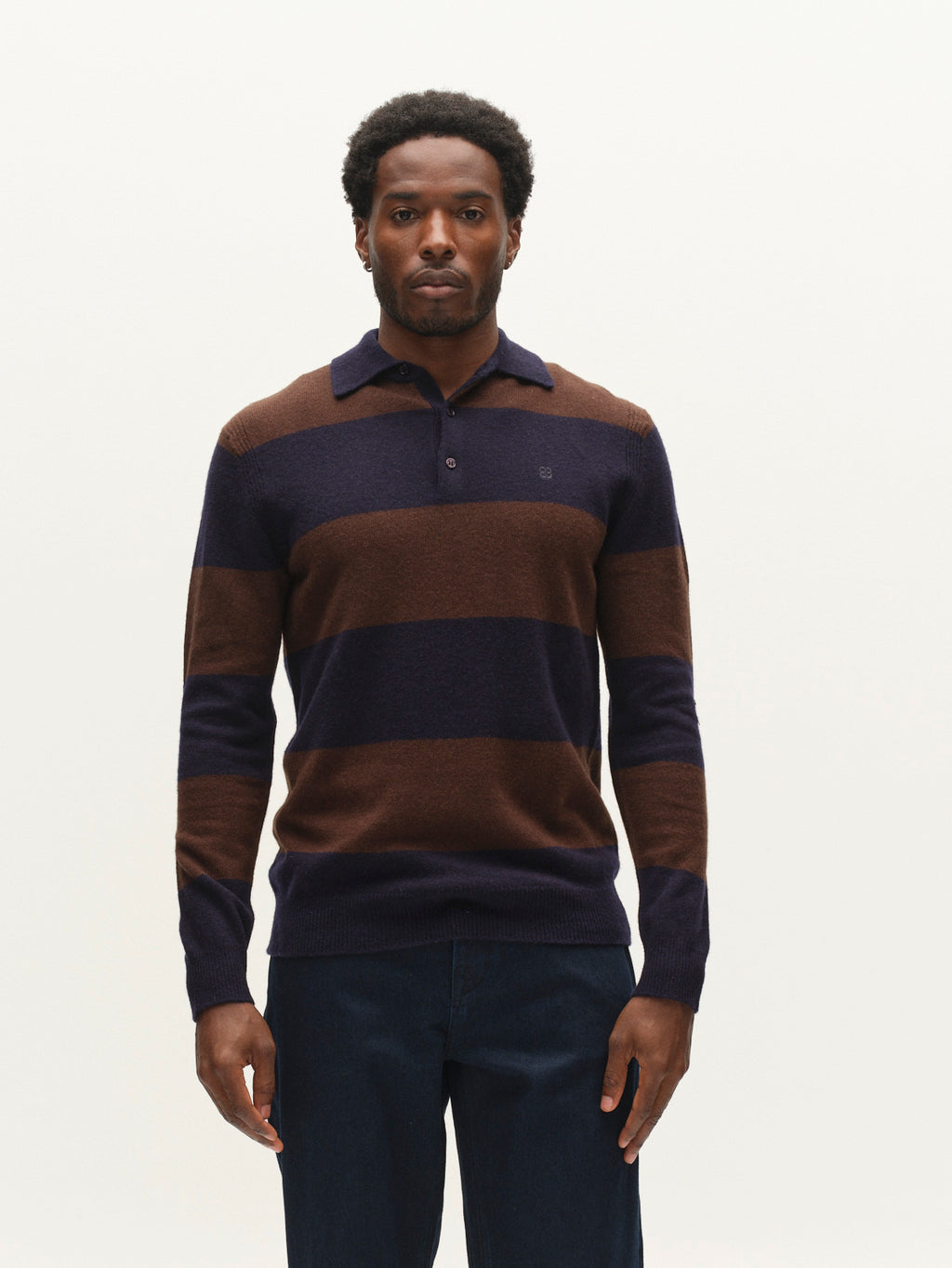 A man stands facing forward, wearing the Gabba GABworren Polo Stripes Aico LS Knit in Brown Stripe and dark pants, against a plain light background.