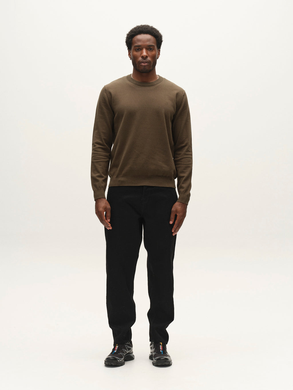 A man stands facing forward against a plain white background, wearing the Gabba GABfumo Element Spy LS Knit in Forest Night—a regular fit, long-sleeve crew neck shirt—paired with black pants and black shoes.