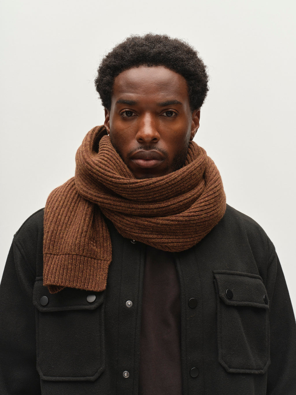 A man wearing the Gabba GABeast Flash Scarf in Brown Slate and a black button-up jacket stands against a plain white background, looking directly at the camera with a neutral expression.