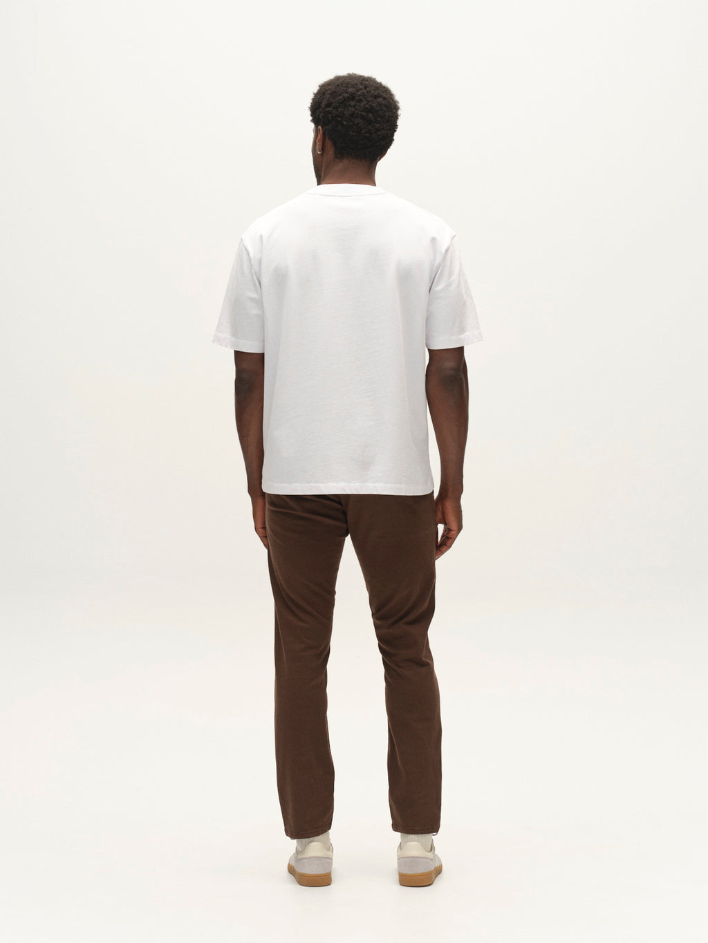 A person stands facing away, wearing a white short-sleeve t-shirt, light-colored shoes, and the Gabba GABpaul K3280 Dale Chino in Brown Slate—crafted from high-stretch cotton-blend fabric—against a plain white background for an effortless everyday look.