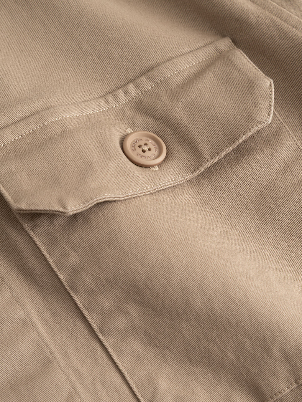 Close-up of a beige fabric pocket with a flap and sewn-on button highlights the stitching details and textured feel of the Gabba GABtopper LS Shirt in Sand Plaza. This heavyweight overshirt features a regular fit, making it a versatile layering essential for any wardrobe.
