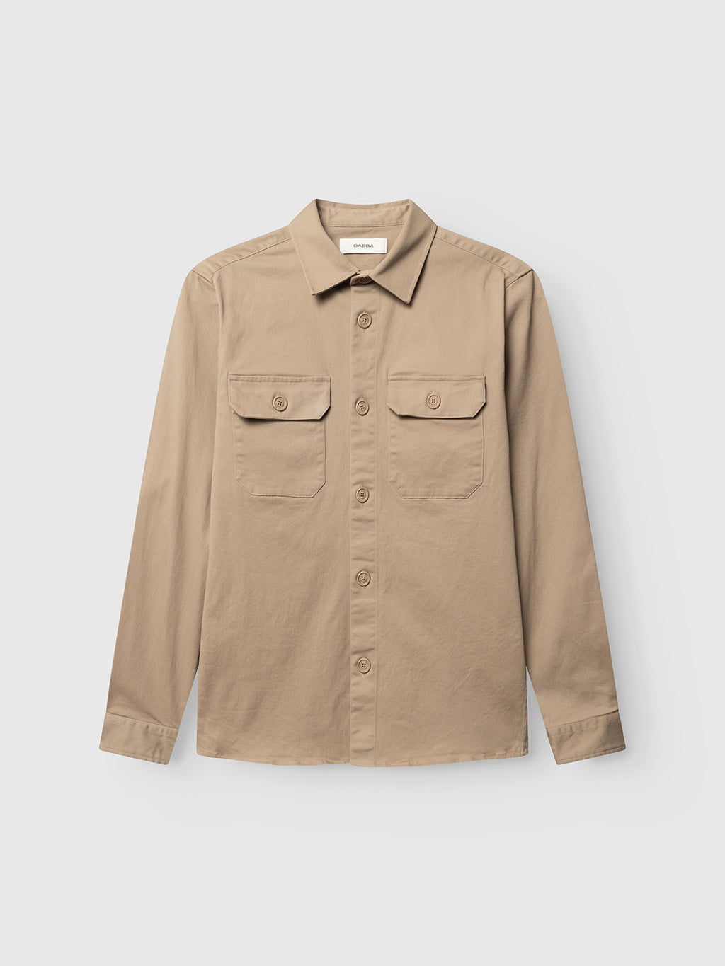 The GABtopper LS Shirt - Sand Plaza by Gabba is a beige, long-sleeve button-up overshirt with two button-flap chest pockets, designed in a regular fit for versatile layering and displayed on a plain white background.