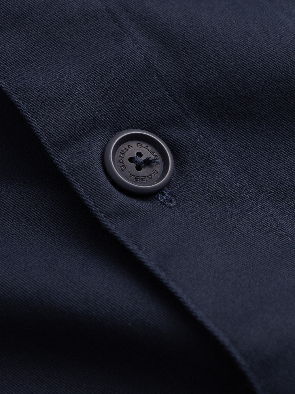 Close-up of the GABtopper LS Shirt - Blue Black by Gabba, showcasing its navy blue fabric and a black button with text around the edge, sewn on with matching dark blue thread. This subtle detail blends seamlessly with the smooth, heavyweight material, emphasizing the shirt’s versatile appeal as an essential layering piece for any regular fit wardrobe.