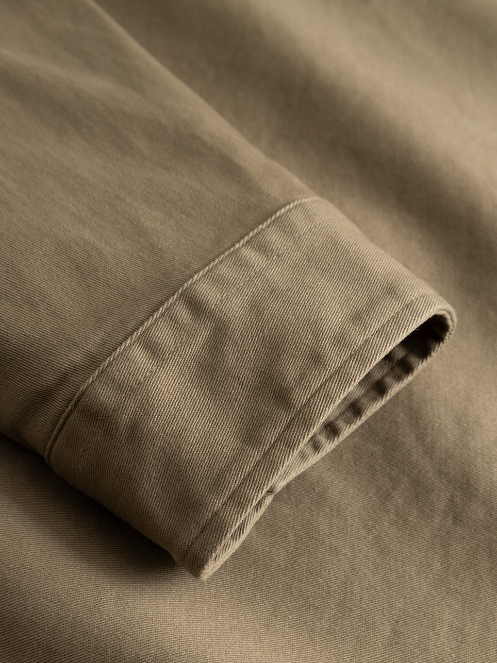 A close-up of the Gabba GABtopper LS Shirt in Dusty Olive highlights the heavyweight sleeve cuff’s detailed stitching and fabric texture, laid flat on a matching background.