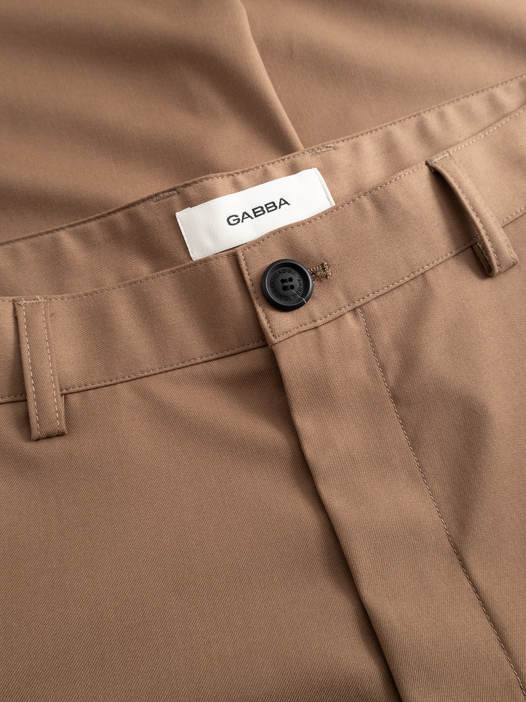 Close-up of Gabba's GABjoe Turnup Fin Pant in sand, showcasing a black button, belt loops, and a white Gabba label above the waistband.