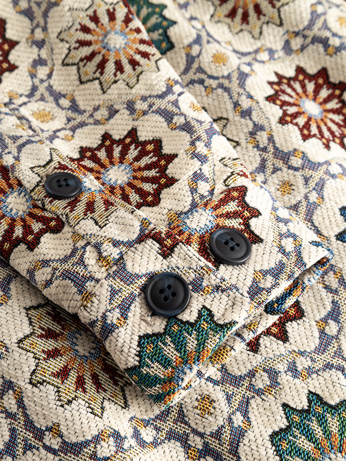 Close-up of the Gabba GABsimone Nava LS - Birch, showcasing jacquard fabric with a geometric floral design in red, green, and blue, and three black buttons sewn onto the material—details likely found on the relaxed fit shirt’s cuff.