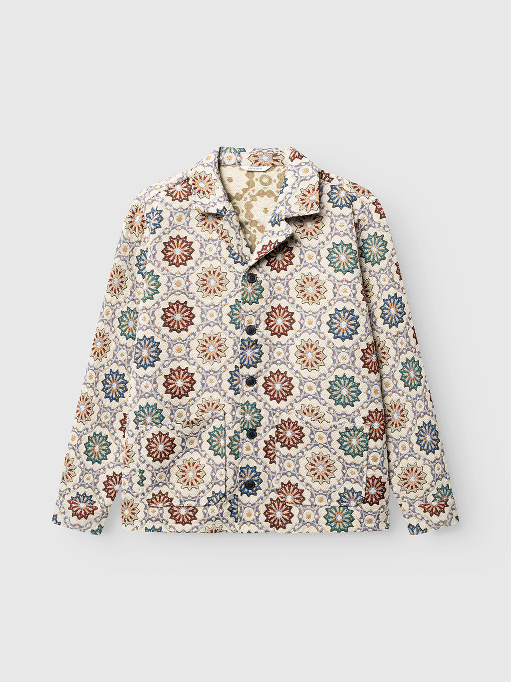 Introducing the GABsimone Nava LS - Birch by Gabba: a relaxed-fit long-sleeve button-up jacket crafted from jacquard fabric, featuring a vibrant floral geometric pattern in red, green, blue, and beige tones on a light background. This jacket seamlessly blends comfort with contemporary style.