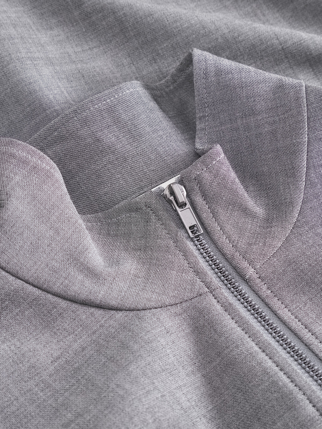 Close-up of the GABnik Phin GRS - Dk. Grey by Gabba, a light gray fabric garment featuring a visible metal zipper and a folded collar that highlight its texture and stitching details. Crafted from a premium wool and viscose blend, this modern outerwear piece is cut in a regular fit.