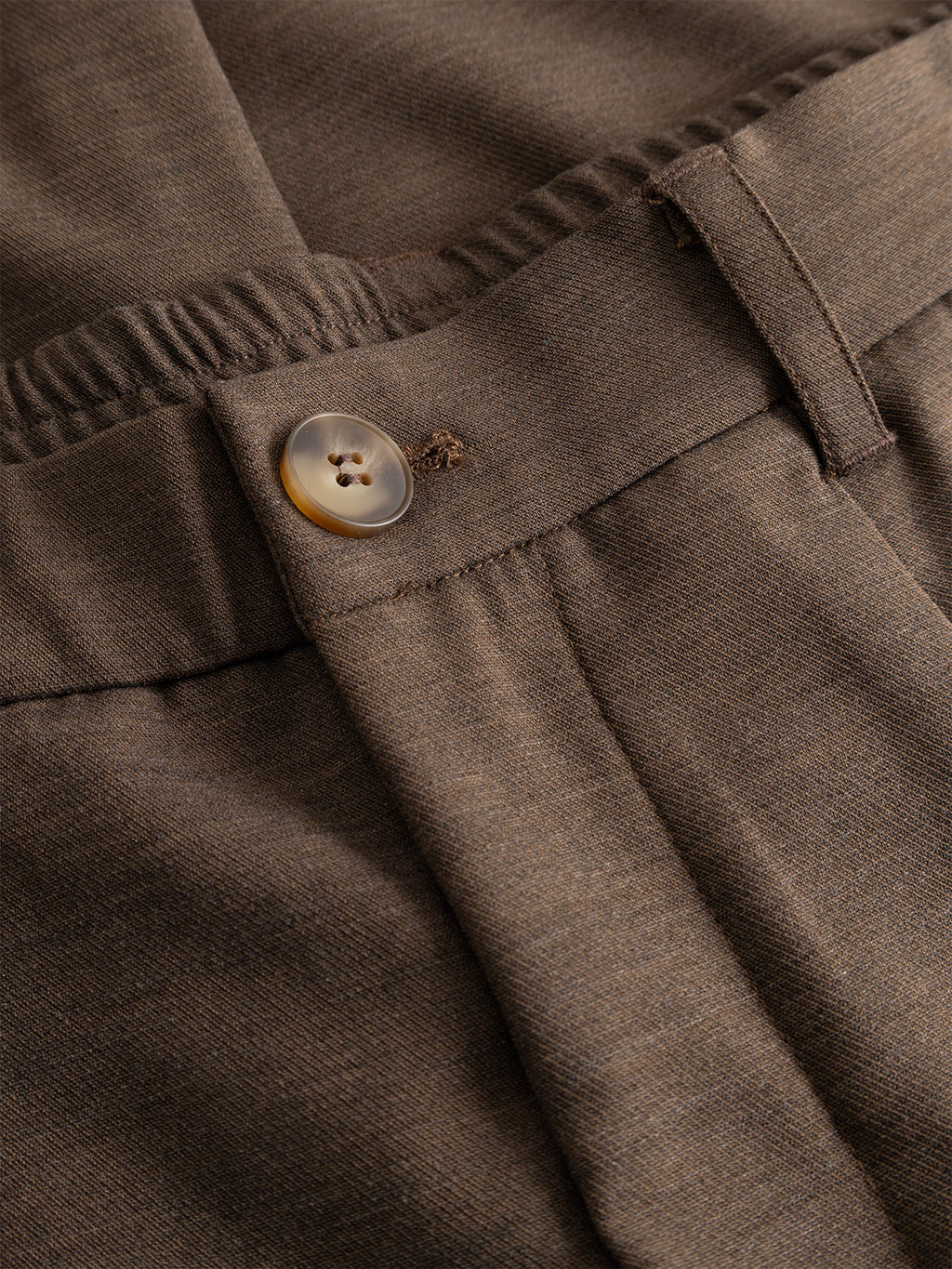 Close-up of Gabba GABnapoli 19 Phin GRS - Crocodile wool blend chino pants, featuring an elastic waistband, belt loop, and a button crafted from brown and cream-colored material.