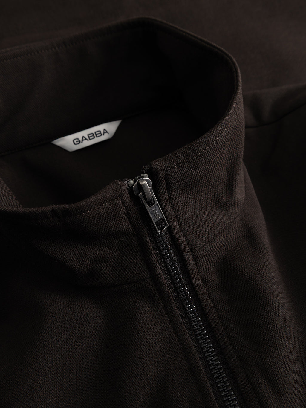 Close-up of the GABnik Phin GRS jacket in Brown Slate by Gabba—crafted from a wool and viscose blend, featuring a visible zipper and a white inner collar tag with the brand name. This modern outerwear piece is perfect as a versatile layering option.