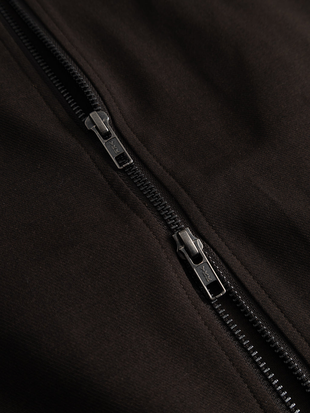 Close-up of a black zipper on dark fabric, showing two zipper sliders positioned closely together along the teeth—a detail that highlights the sleek functionality of the Gabba GABnik Phin GRS - Brown Slate outerwear, expertly crafted from a wool and viscose blend.