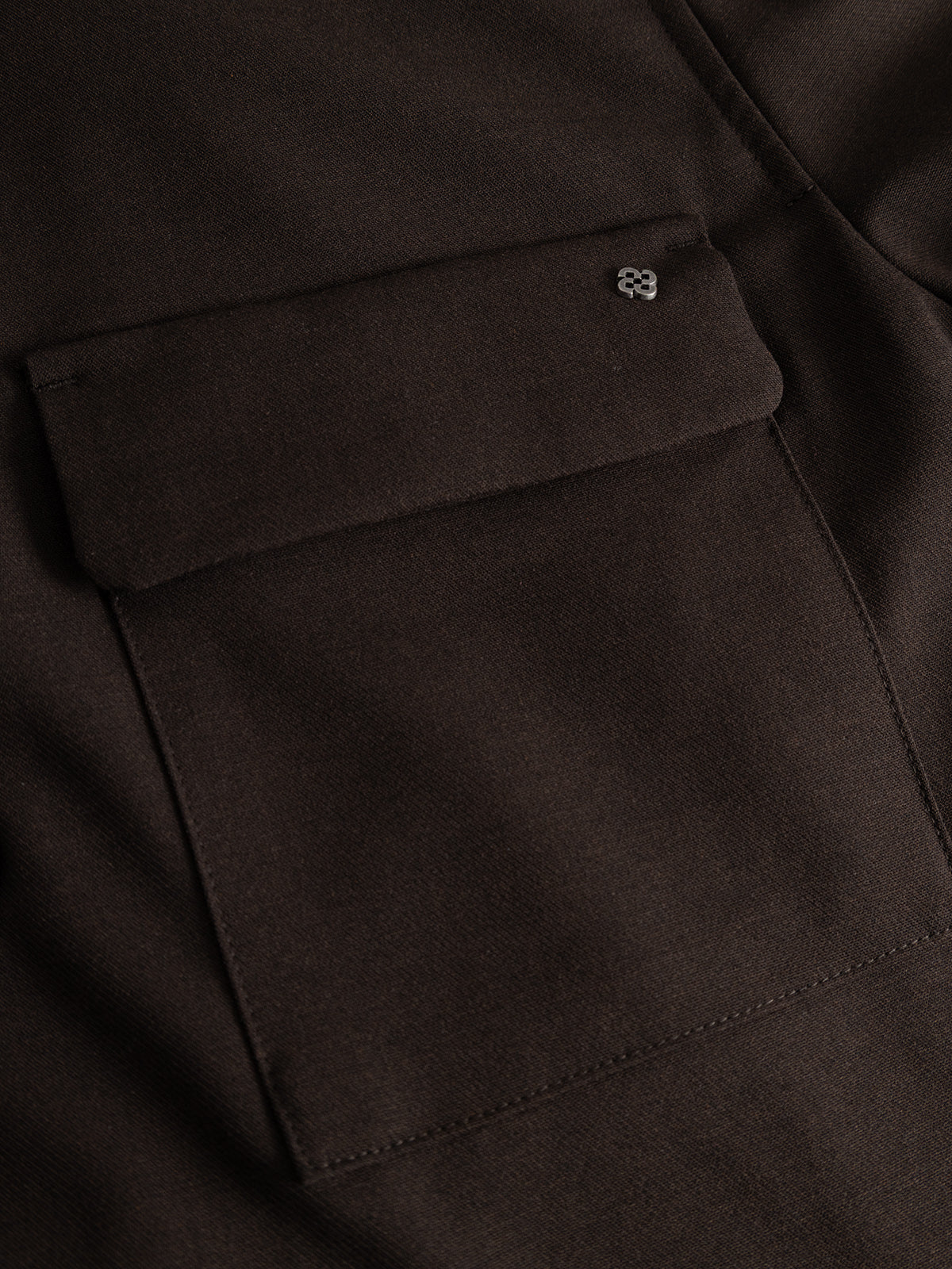 Close-up of the GABtogger Push Phin LS Overshirt GRS by Gabba in Brown Slate, showcasing a dark brown fabric pocket with a flap and a discreet metallic logo pin on the upper right corner. Crafted from a smooth yet durable wool-viscose blend, this overshirt is an ideal layering essential.