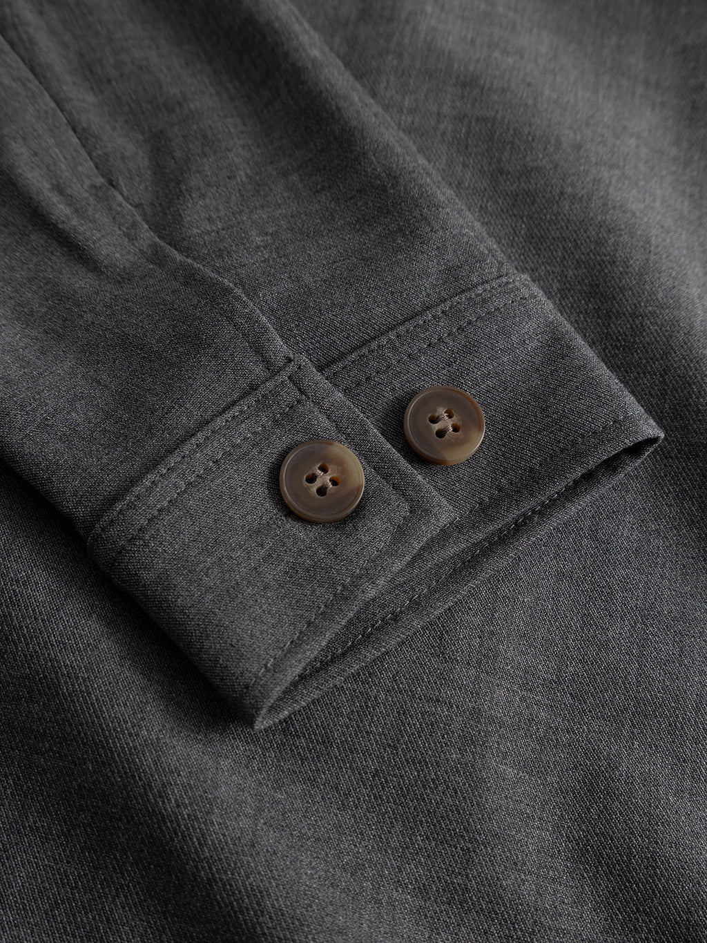 Close-up of the Gabba GABtogger Push Phin LS Overshirt GRS in dark grey, featuring a long-sleeve cuff with two brown buttons on softly textured fabric—a layering essential made from a comfortable wool-viscose blend in a regular fit.