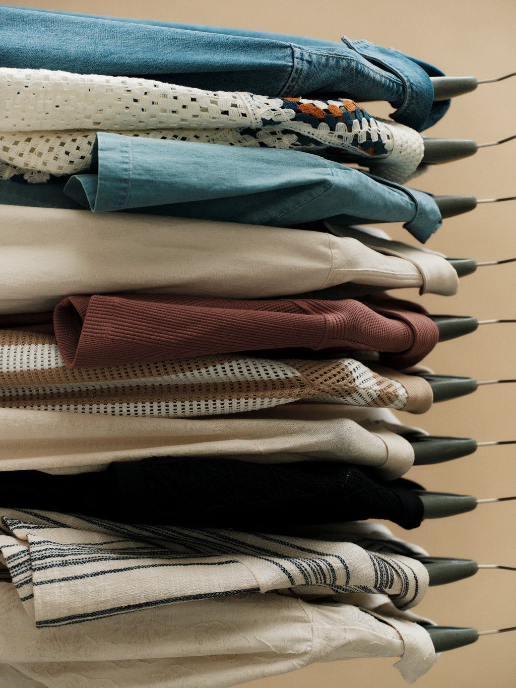 A side view of neatly stacked hangers displays shirts and blouses in various fabrics and colors, including the Gabba GABjens Over Resort Riga SS Shirt in Navy Stripe.