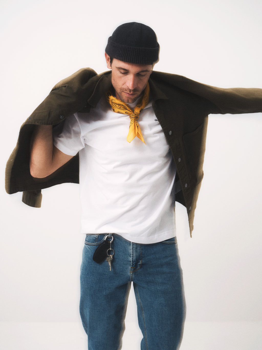 A man in a modern slim fit olive green jacket, white t-shirt, and Gabba GABmax Cros - Lt. Blue Denim jeans stands against a plain background. His clean look is topped with a black beanie and yellow bandana—Max Cros-approved style.