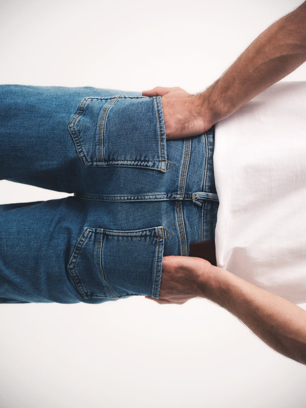 A person is seen from behind wearing Gabba’s GABmax Cros - Lt. Blue Denim jeans and a white shirt, hands in their back pockets. The photo, cropped at the waist and thighs, highlights the jeans’ clean slim fit look.