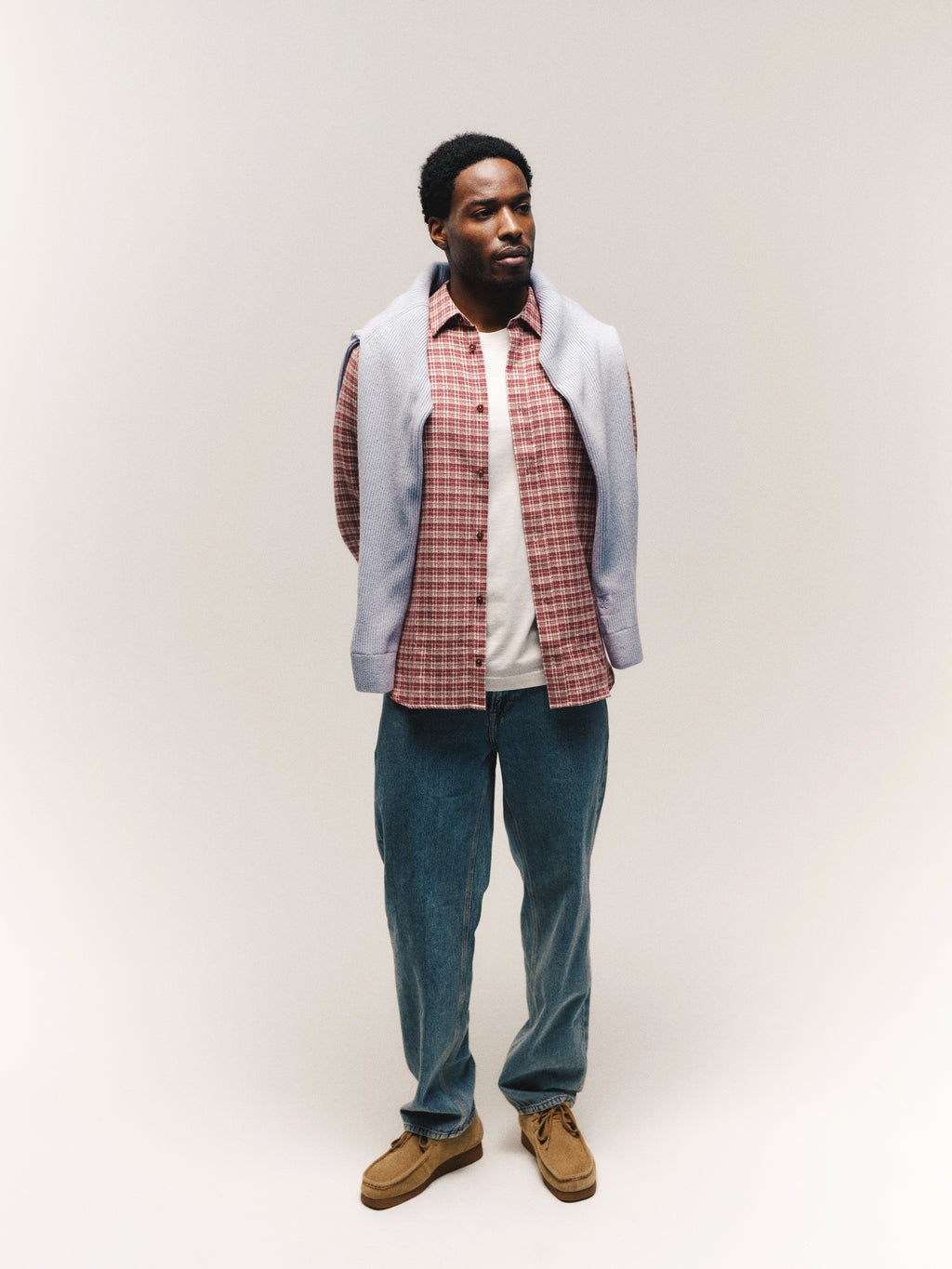 A man stands against a plain background wearing the Gabba GABsven Reg TX2 LS Shirt in Brick Red over a white T-shirt, blue jeans, brown shoes, and a light blue sweater draped over his shoulders.
