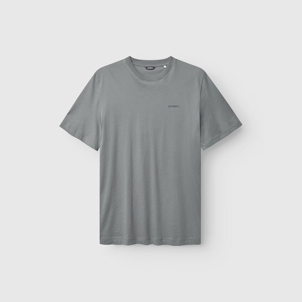 The Gabba GABdune Logo SS GOTS in Dust Sage Green is a short-sleeved organic cotton t-shirt with a crew neckline and a subtle logo on the left chest, shown on a light gray background.